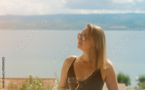 Woman enjoys rose wine on seaside balcony.