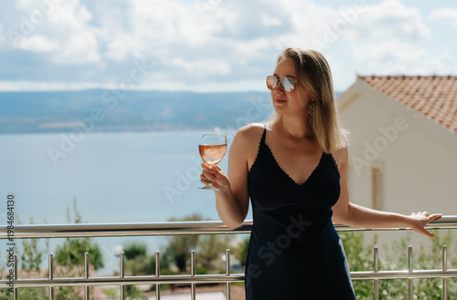 Woman enjoys rose wine on seaside balcony.