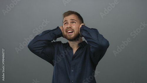 Bild auf Leinwand Young caucasian man pressing hands over ears and wincing in gray studio wearing navy shirt; pain noise sensitivity