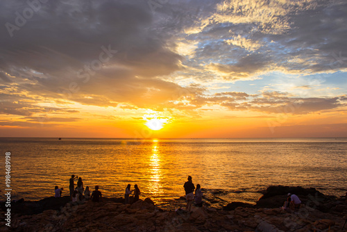 The sunset is reflected on the water surface with tourists taking pictures of the scenery at Khao Laem Ya viewpoint in Rayong Province, Thailand.