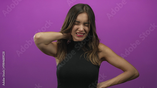 Obraz na plátně Woman holding neck in studio against vibrant purple backdrop with eyes closed in apparent pain and tense expression; discomfort