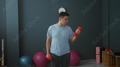 Wallpaper Mural Man lifting red dumbbell with right hand in studio performing bicep curl; strength focus determination. Torontodigital.ca