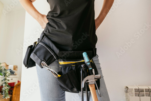 Close-up of an anonymous woman doing home renovations with a tool belt and tools