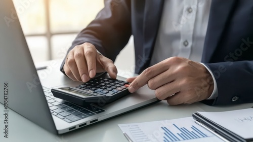 Person using a calculator and laptop to analyze financial data shown on printed charts.