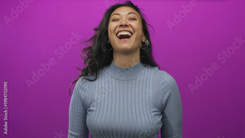 Canvas Print Woman young laughing with hand covering face and open mouth in purple studio wearing blue sweater; joy confidence
