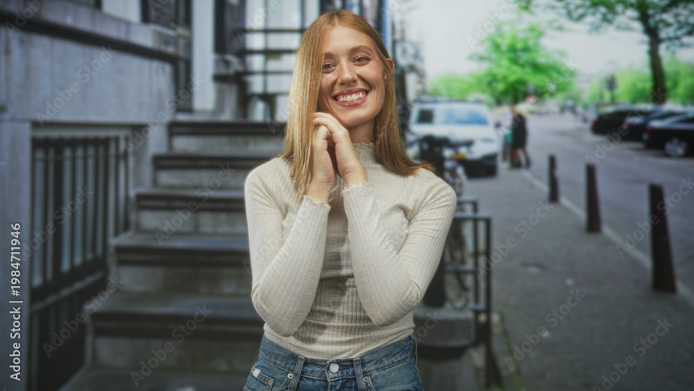 Fototapeta premium Woman clasping hands near chin smiling on stone steps by sidewalk with parked cars on city street; gentle joy.