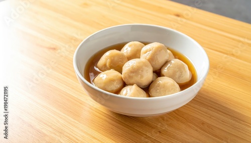 Plump Glistening Fishballs Steamed in Savory Broth Served in a White Bowl on a Wooden Surface