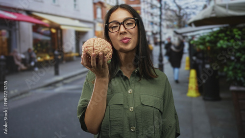 Wallpaper Mural Hispanic woman in glasses holds a brain model in one hand on a busy city street, smiling and offering it toward camera; curiosity insight. Torontodigital.ca