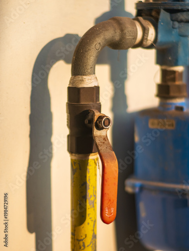 Close-up of industrial metal pipe with valve handle connected to a utility system, highlighted by warm sunlight, representing infrastructure, plumbing, and mechanical equipment.