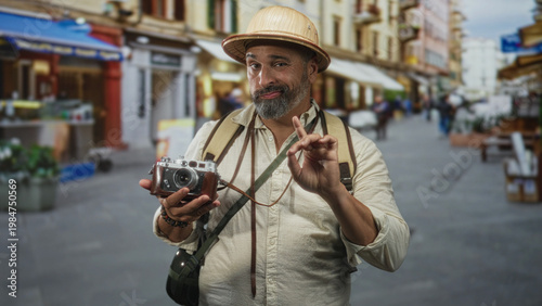 Canvas Print Man holding vintage camera and pointing finger on a street market with backpack and pith helmet visible; curious traveler moment