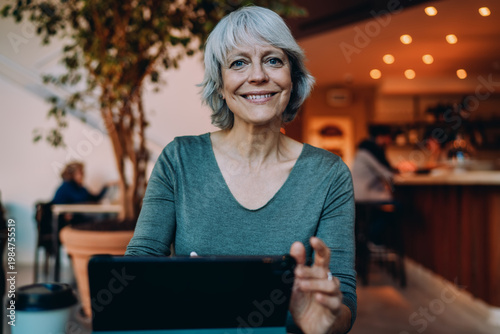 Obraz na plátně Smiling gray-haired woman using tablet at café table, enjoying screen interaction