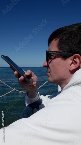 Young man at the beach using smartphone for voice message, chatting with AI.