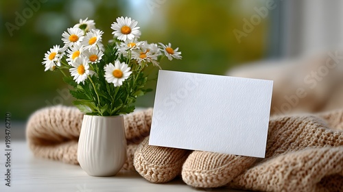 Daisies in vase with blank greeting card on knitted sweater