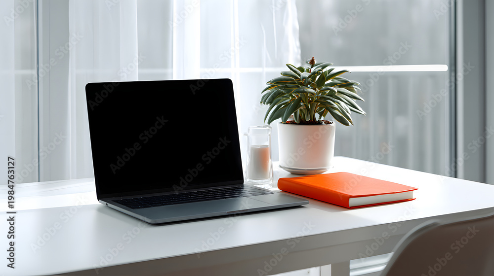 Fototapeta premium Clean white desk with laptop, orange notebook, potted plant and candle by bright window creating calm workspace atmosphere