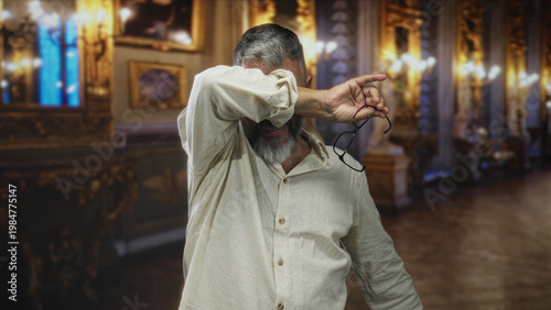Foto Middle aged man covering face with hand while holding glasses in building museum gallery; privacy avoidance embarrassment