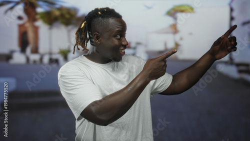 Foto Man gesturing with hands on a street wearing a white t shirt, smiling with open mouth with palm trees and steps behind; joyful energy