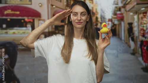 Canvas Print Woman holding a yellow rubber duck and saluting with hand to forehead on a busy street market; playful innocence