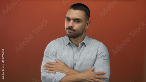Obraz na płótnie Hispanic man wearing striped shirt crosses arms in orange studio while closing eyes; rejection introspection