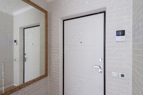 Modern apartment entrance with white door, mirror and intercom, clean hallway interior
