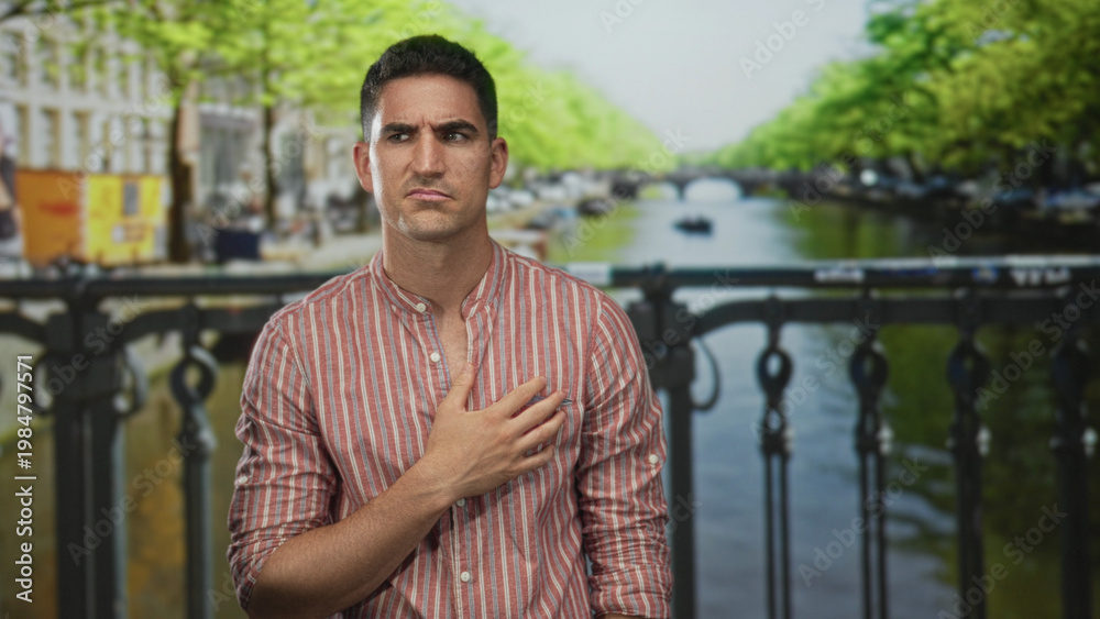 Fototapeta premium Man clutching chest for heartattack on street in amsterdam by canal bridge, striped shirt visible; pain vulnerability.