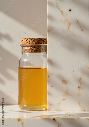 Glass jar with cork lid filled with golden oil on marble background  