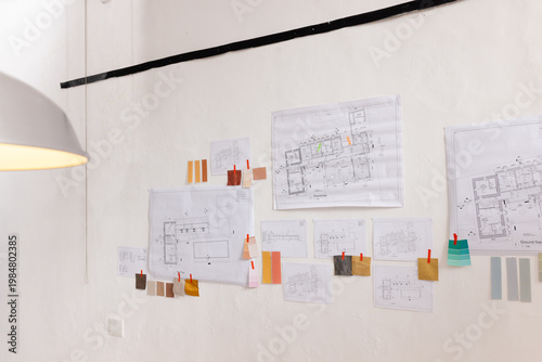Pinning architectural plans, swatches and red clips on design studio pin-up wall under pendant lamp