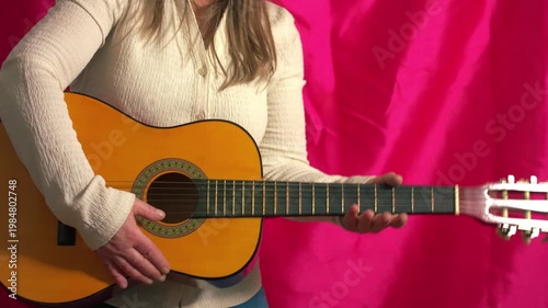 Woman playing acoustic guitaron pink background