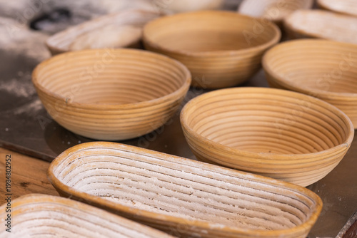 Coiled rattan bannetons sitting on wooden bench in bakery, showing flour dusting grooves