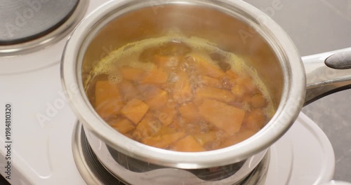 Stainless-steel saucepan on kitchen hob heating water, orange cubes bubbling and softening