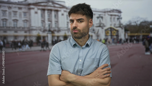 Foto Man with crossed arms and bare forearm standing on a crowded city street in front of a palace building; defiance