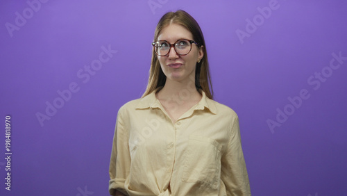 Valokuva Blonde woman wearing glasses sticks out tongue, raises hands and smiles while tilting head in purple studio; mischief