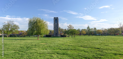 Panoramic view of the historic Joseph Dill Baker Carillon tower in Baker Park, Frederick, Maryland, surrounded by a lush green lawn under a clear blue sky.