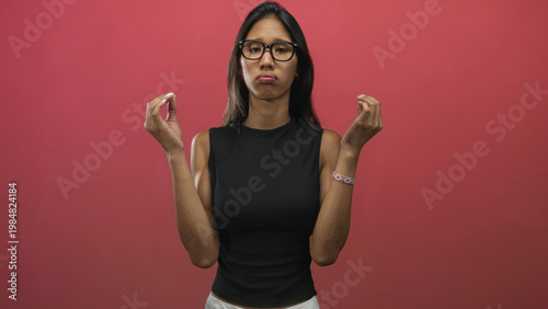 Canvas Print Thai woman in black sleeveless top pinches fingertips with raised hands showing bare forearms and glasses in studio; exasperation introspection
