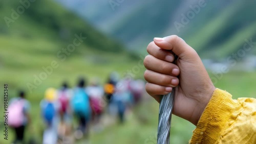 Tracking shot of hand gripping walking stick leading group hiking along mountain valley trail in green countryside during daytime