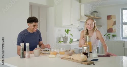 Couple starting breakfast at kitchen island as woman pouring orange juice, man cutting bread