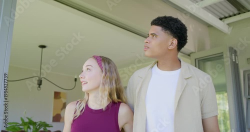 Diverse couple at glass door spotting outdoors, pointing, leaning, waving red-tag keys celebrating