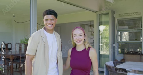 Diverse couple walking through glass doors at home after opening turning to camera man raising keys