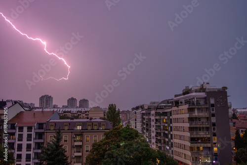 Foto Dramatic pink lightning bolt striking across a purple stormy sky above a modern cityscape with illuminated apartment buildings during twilight