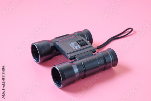 Black and small binoculars on color background.
