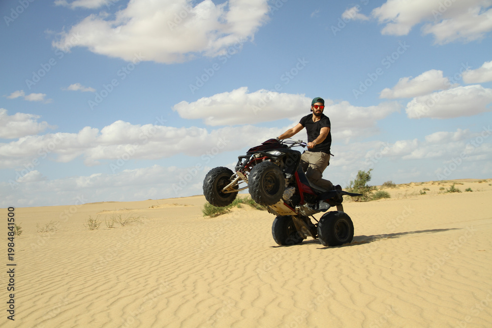 Obraz premium Young quad bike rider doing wheelie in desert