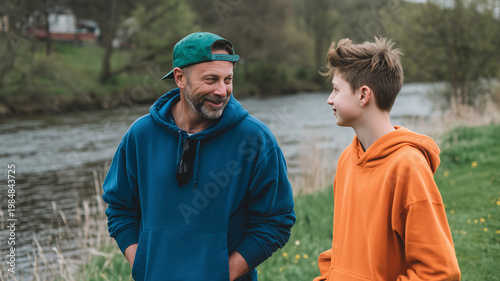 A man in his late thirties with short black hair and a beard, wearing a blue hoodie, is talking to an older teenage boy. Ai generated