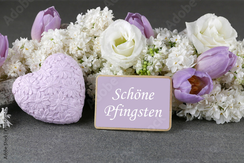 Grußkarte Schöne Pfingsten: Stillleben mit weißem Flieder, Tulpen und violettem Herz mit Schriftzug 'Schöne Pfingsten'.“
