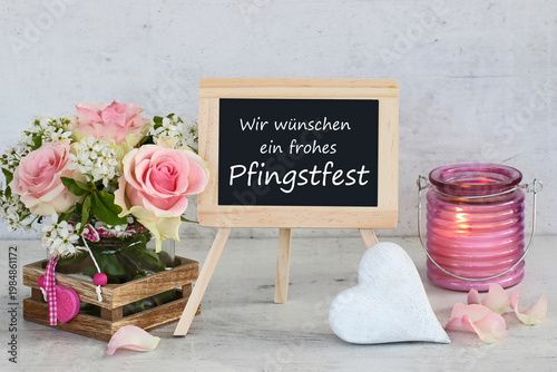 Herzliche Pfingstgrüße: Stillleben mit Rosen, brennendem Windlicht und Tafel  mit dem Text Wir wünschen ein frohes Pfingstfest.