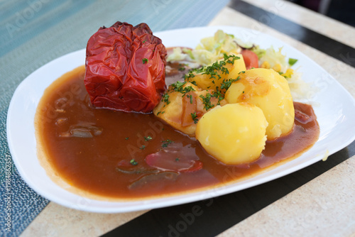 Overcooked stuffed red bell pepper with potatoes, lettuce, and plenty of brown sauce, traditional dish served on a plate at a casual dining restaurant, Germany, selected focus