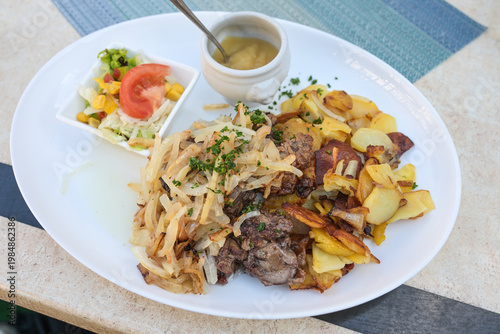 Fried chicken liver with onions, fried potatoes, salad and a bowl of mashed apples, traditional dish in Germany, selected focus