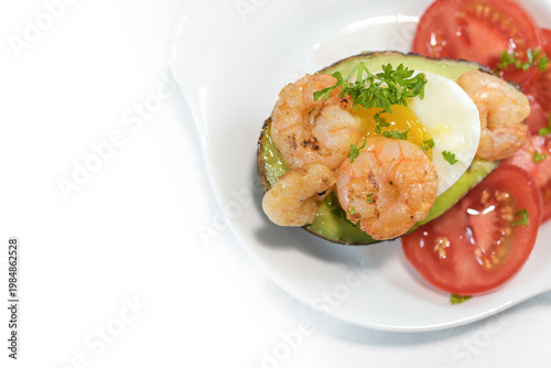 Roasted shrimps and a boiled egg on an avocado with tomato and parsley garnish, tasty snack for breakfast or brunch, nearly white background, top view from above, copy space