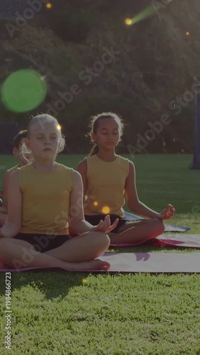 Two girls sitting on yoga mats following cue, breathing while green flare bokeh drifting over them