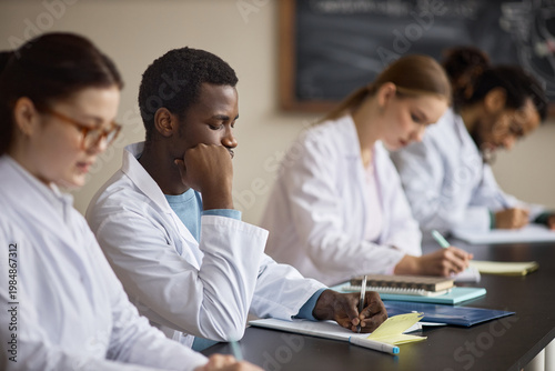 Multiethnic medical students taking notes during classroom training, preparing for healthcare careers and clinical exams. Useful for education marketing, medical school promotion