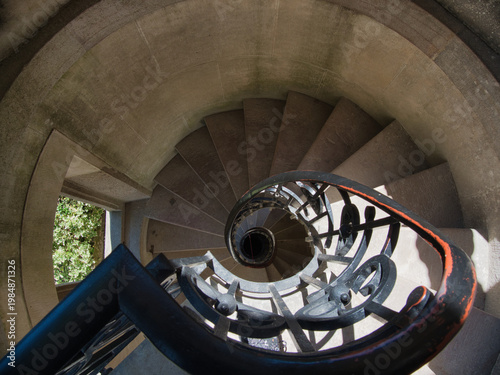 Architectural Spiral Staircase View Down - Striking overhead view of a historic spiral stone staircase with a dark wrought iron railing, emphasizing dizzying architectural geometry and ascent/descent.