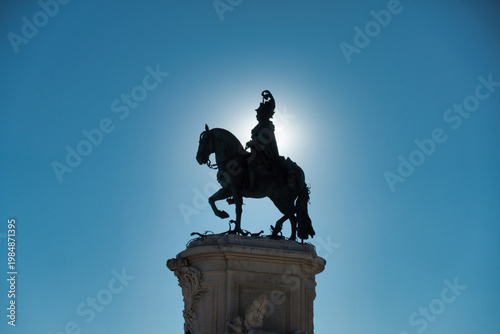 Obraz na plátně Dramatic low-angle silhouette of the bronze equestrian statue of King Jose I in Lisbon's Praça do Comércio, featuring a striking sunburst against a bright blue sky